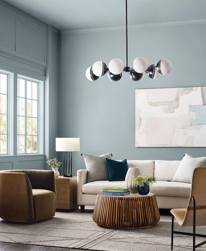 tall light blue painted walls with wall molding around the window, a cream sofa and statement modern black chandelier