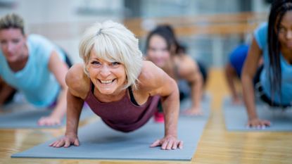 A woman with gray hair smiles as she does yoga.