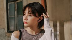 A young woman with a thoughtful expression is listening to Sennheiser Accentum Open earbuds in front of an old-looking residential building