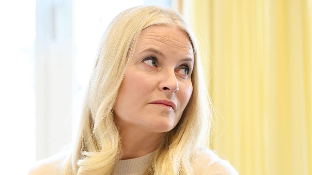 Crown Princess Mette-Marit wearing a cream sweater sitting in front of a yellow background