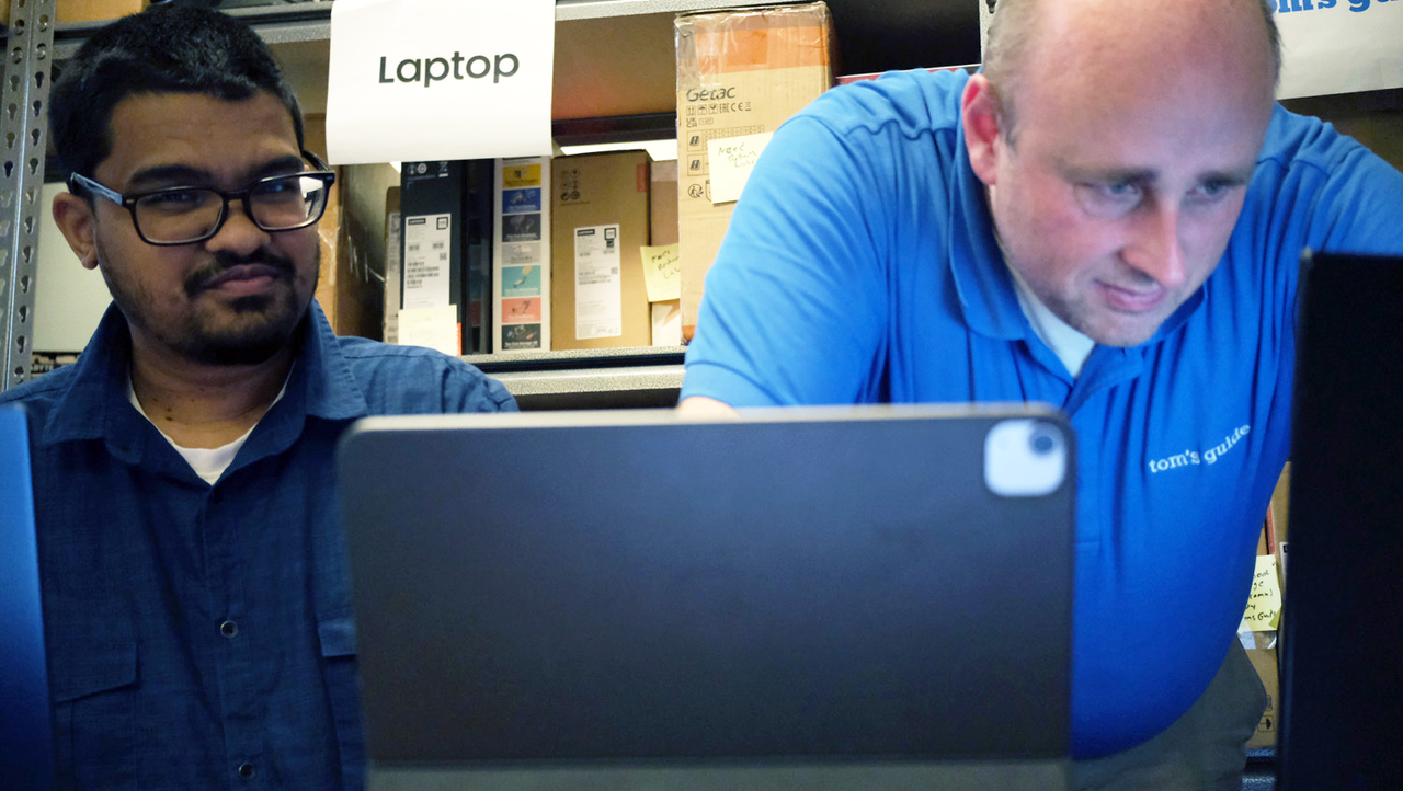Two people standing over a tablet and laptop in the Laptop Mag testing lab.
