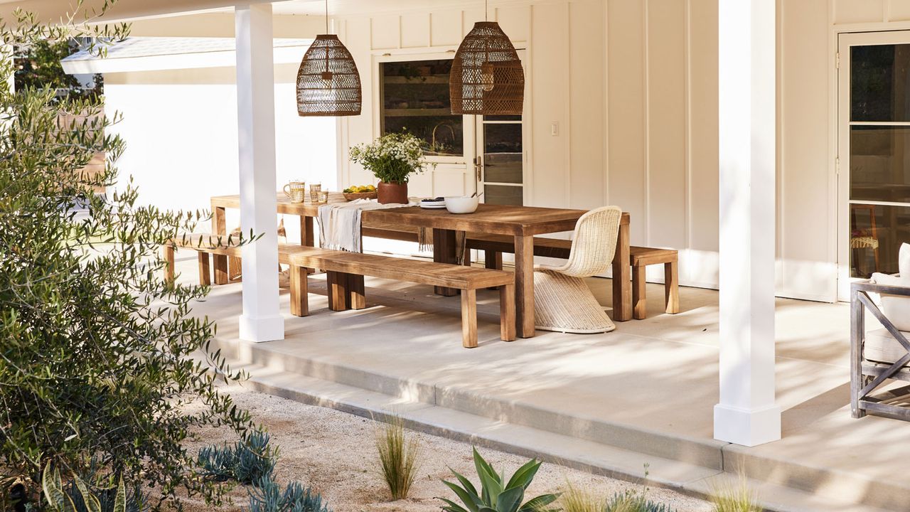 covered outdoor dining area with table and benches, hanging lanterns and accessories, with gravel landscaping and planting