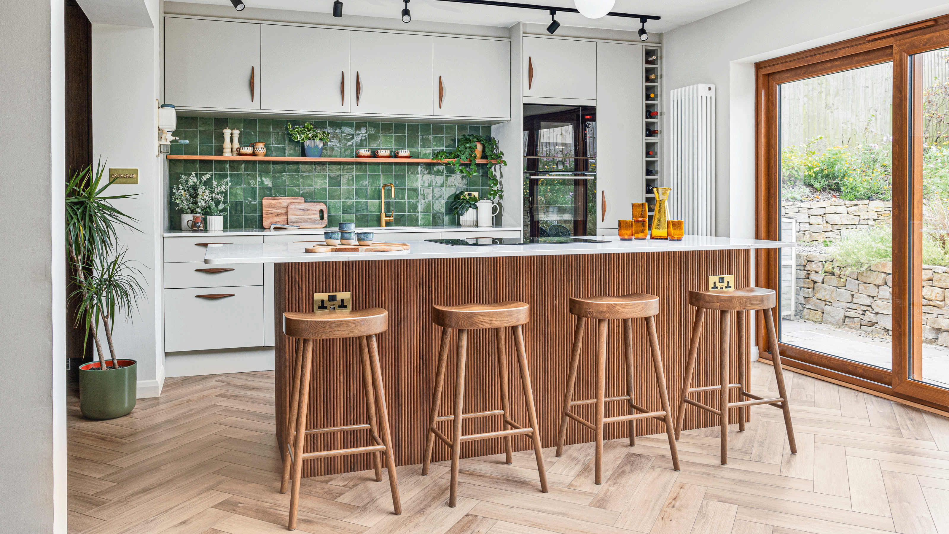 a kitchen with white cabinets, a green tiled splashback and a wooden fluted kitchen island and wooden bar stools