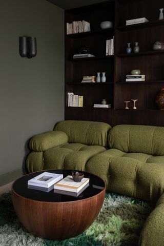 A sage green living room with green sofa, dark wood bookcase and circular coffee table