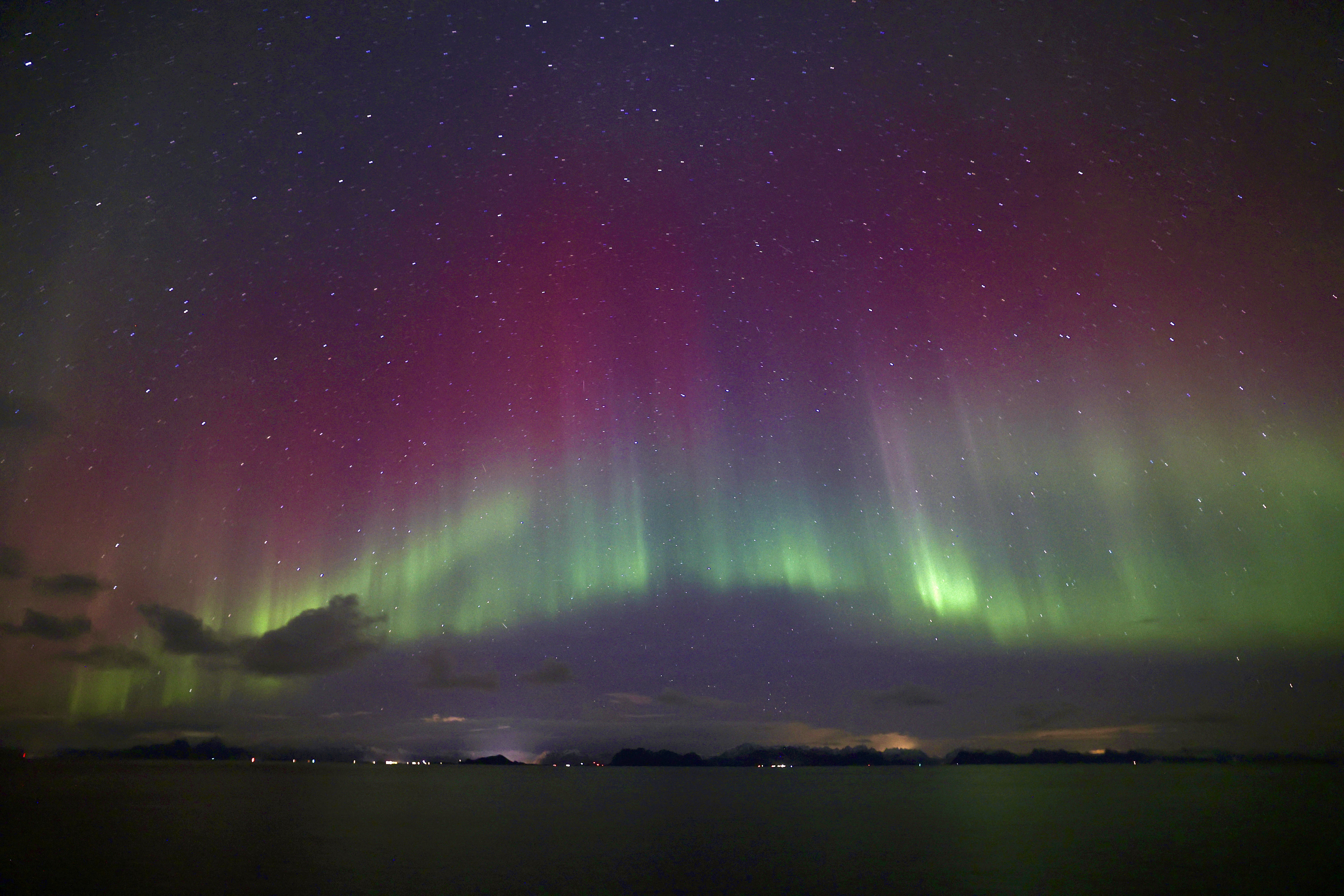 northern lights appear as green and magenta curtains of light in the sky with water below.