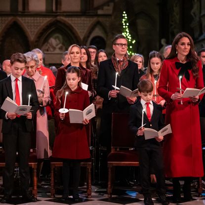 Prince George, Princess Charlotte, Prince Louis and Kate Middleton wearing red and blue dress clothes in church holding candles and singing