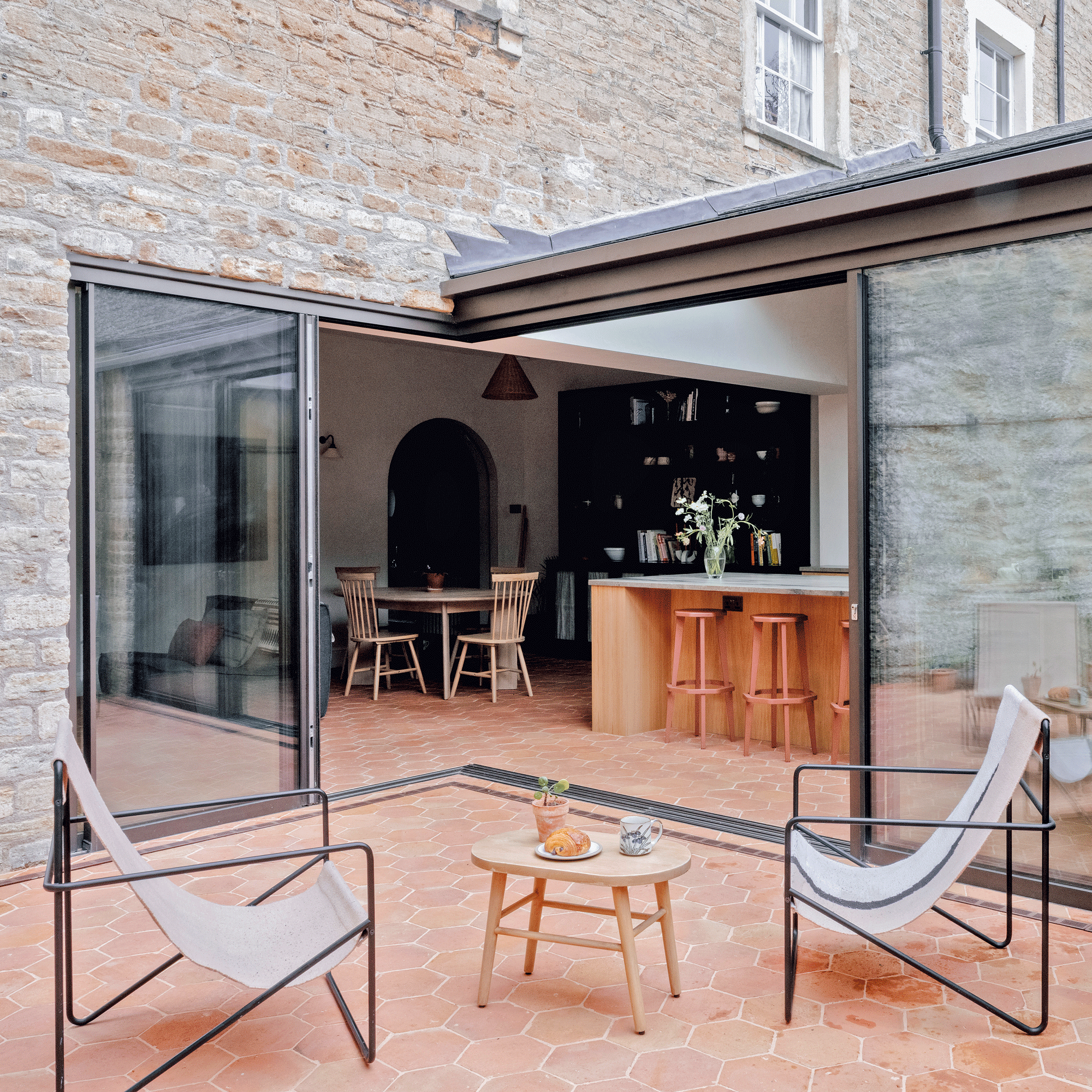 the view into an open plan kitchen from a small patio courtyard with a set of two lounging chairs