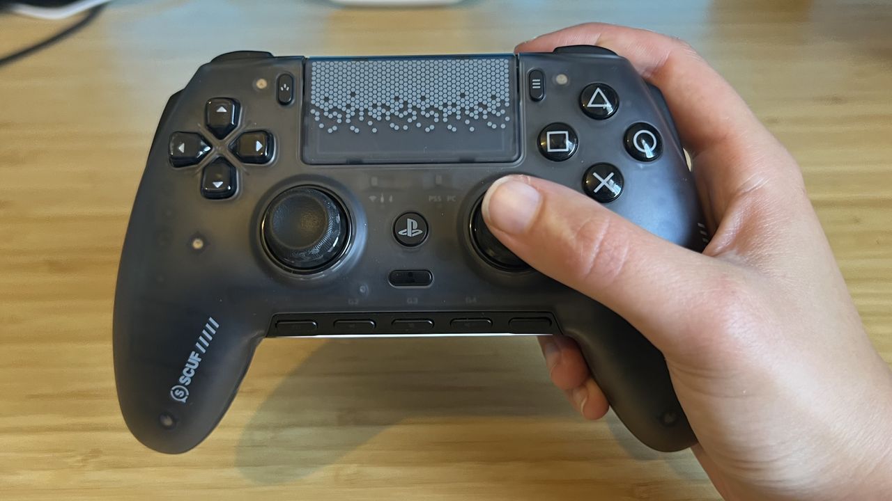 Hand holding the Scuf Omega PS5 controller against a wooden desk