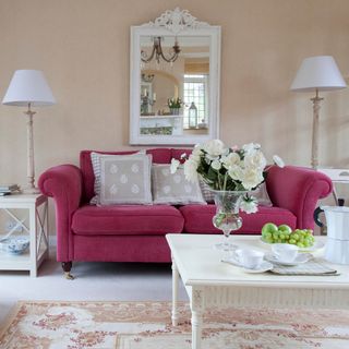 A neutral living room with hot pink sofa with cushions and vintage wall-mounted mirror