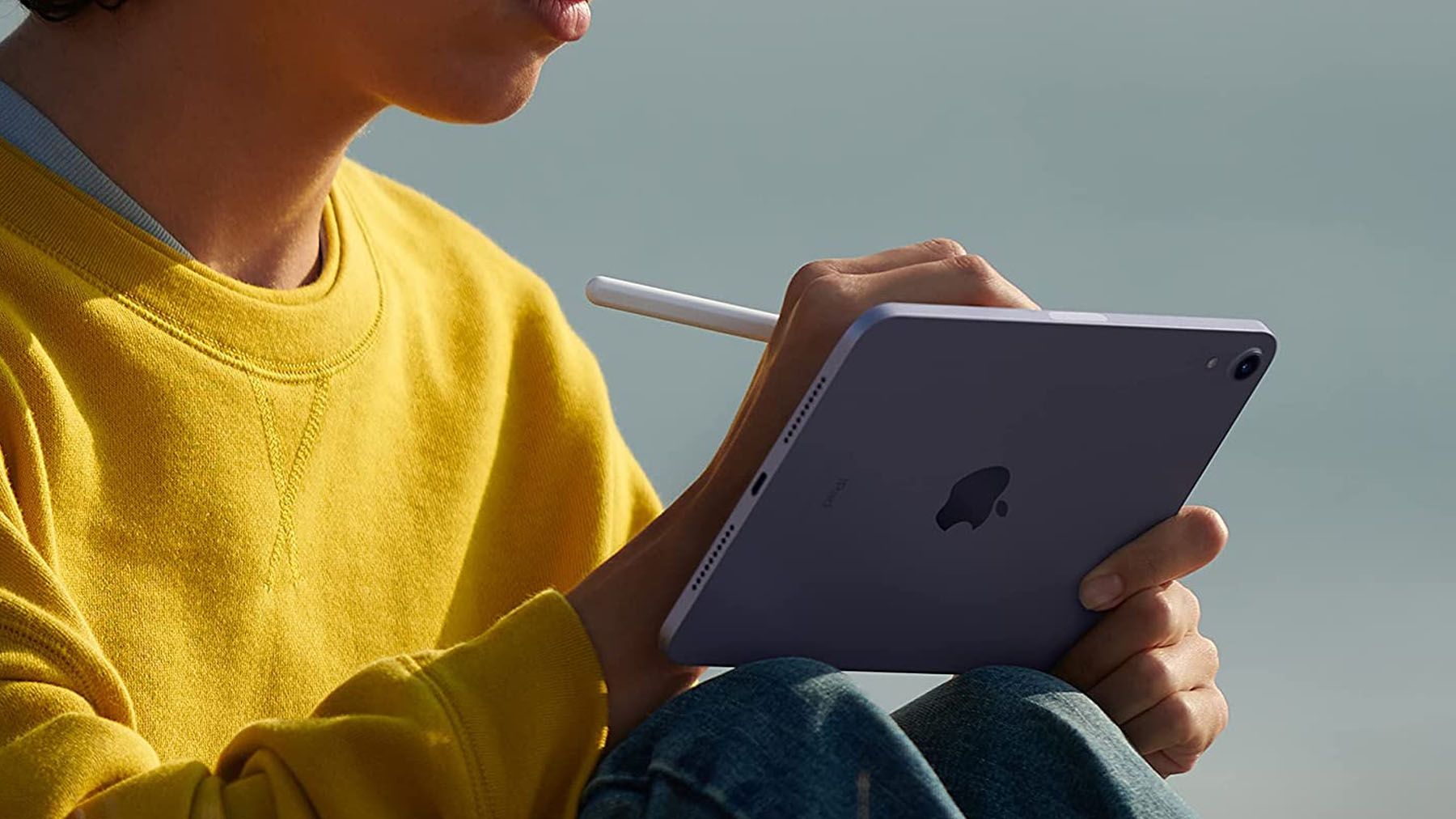 A photo of someone sitting on an iPad Mini while using an Apple Pencil