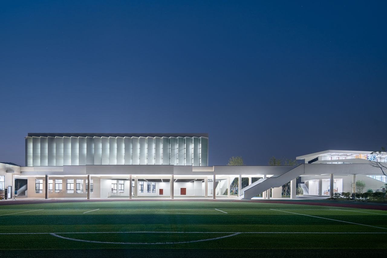 A night view of a sports field with a white double storey school building behind it.