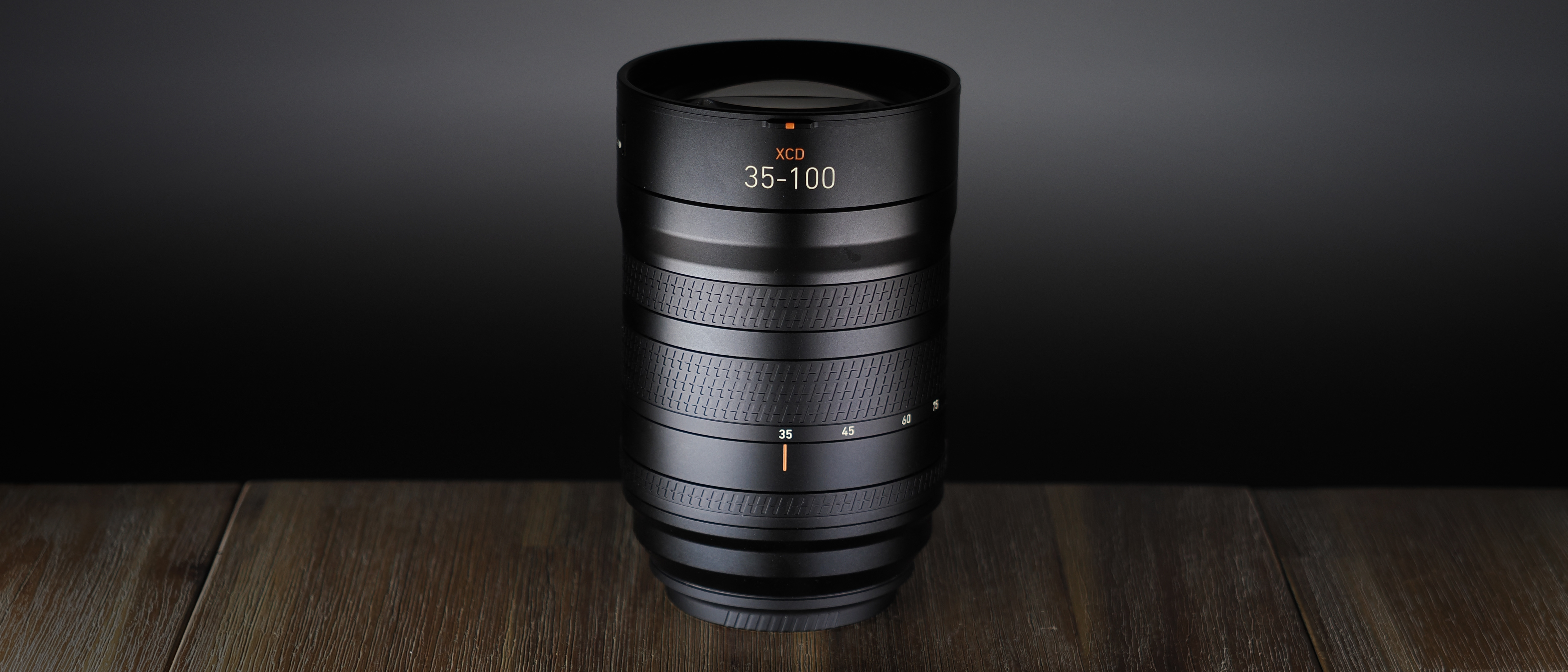 Hasselblad XCD 35-100E lens on a wooden surface in a moodily lit environment