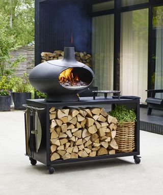A Morso pizza oven on a wheelie trolley stand with wood logs