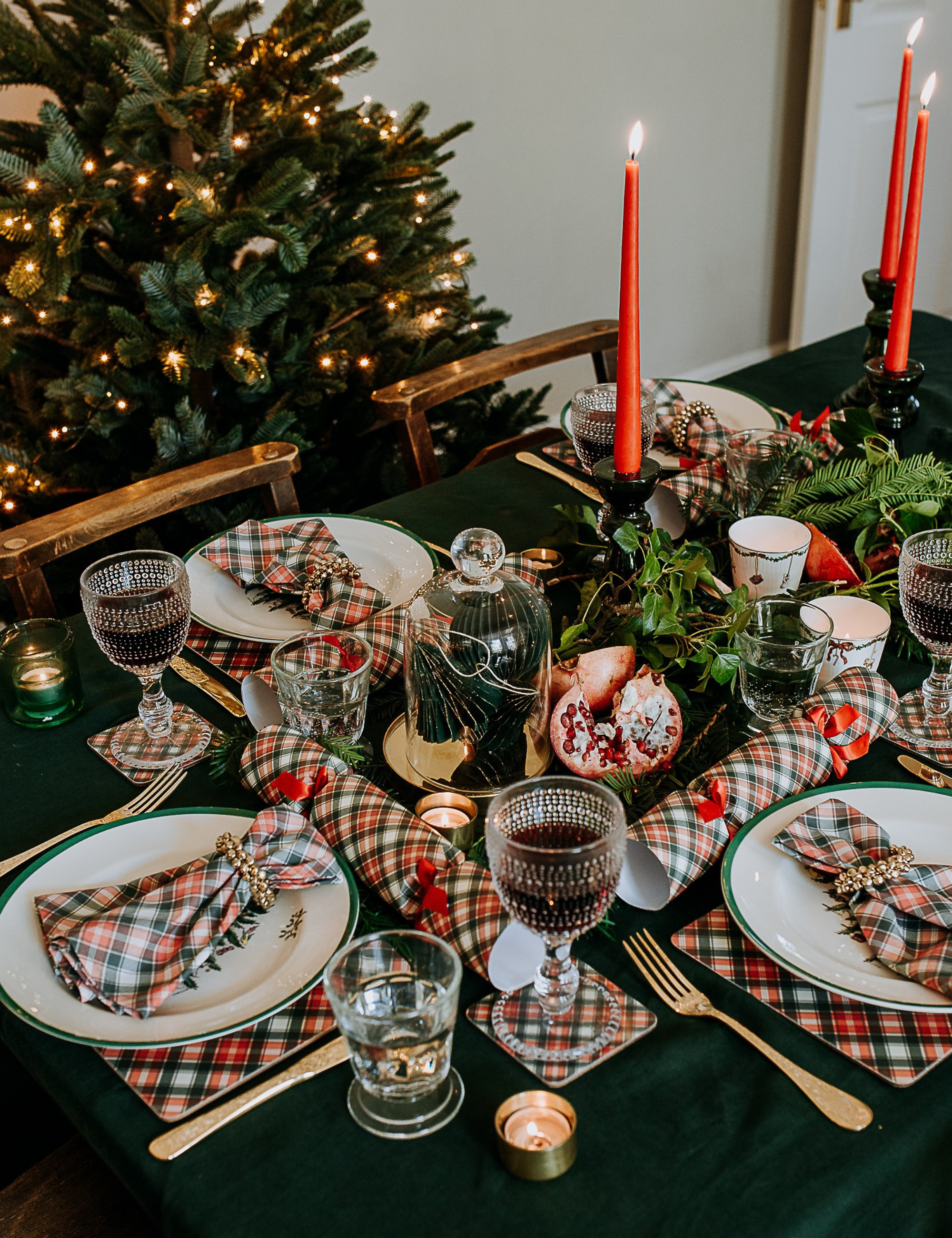 Ralph Lauren Christmas tablescape featuring hunter green and tartan table linens, red taper candles, and brass flatware.