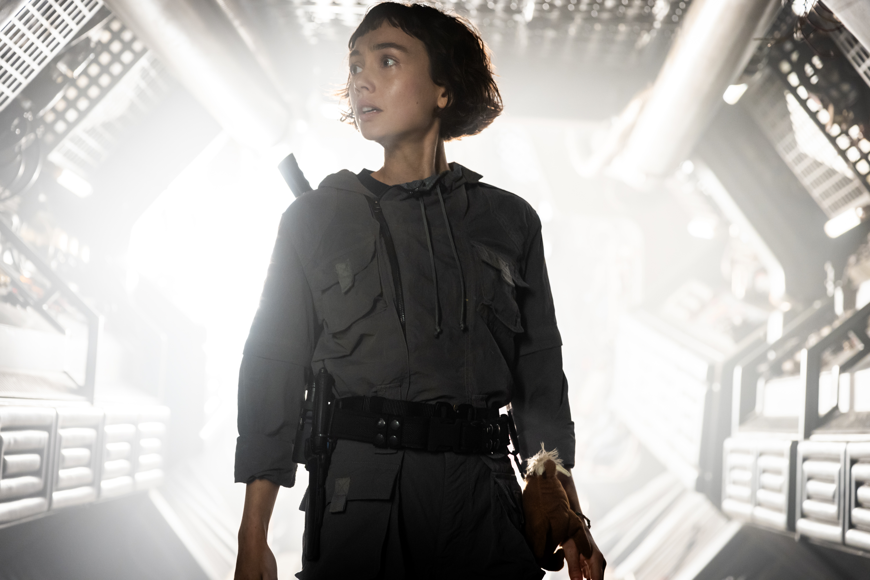 A woman stands outside a spaceship looking off camera.
