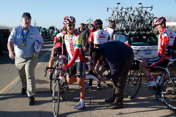 Minutes before stage start, overall race leader Patrick Bevin (Bissell) gets a cleat adjustment as USAC official Tom Simonson heads to the commissarie's lead vehicle.