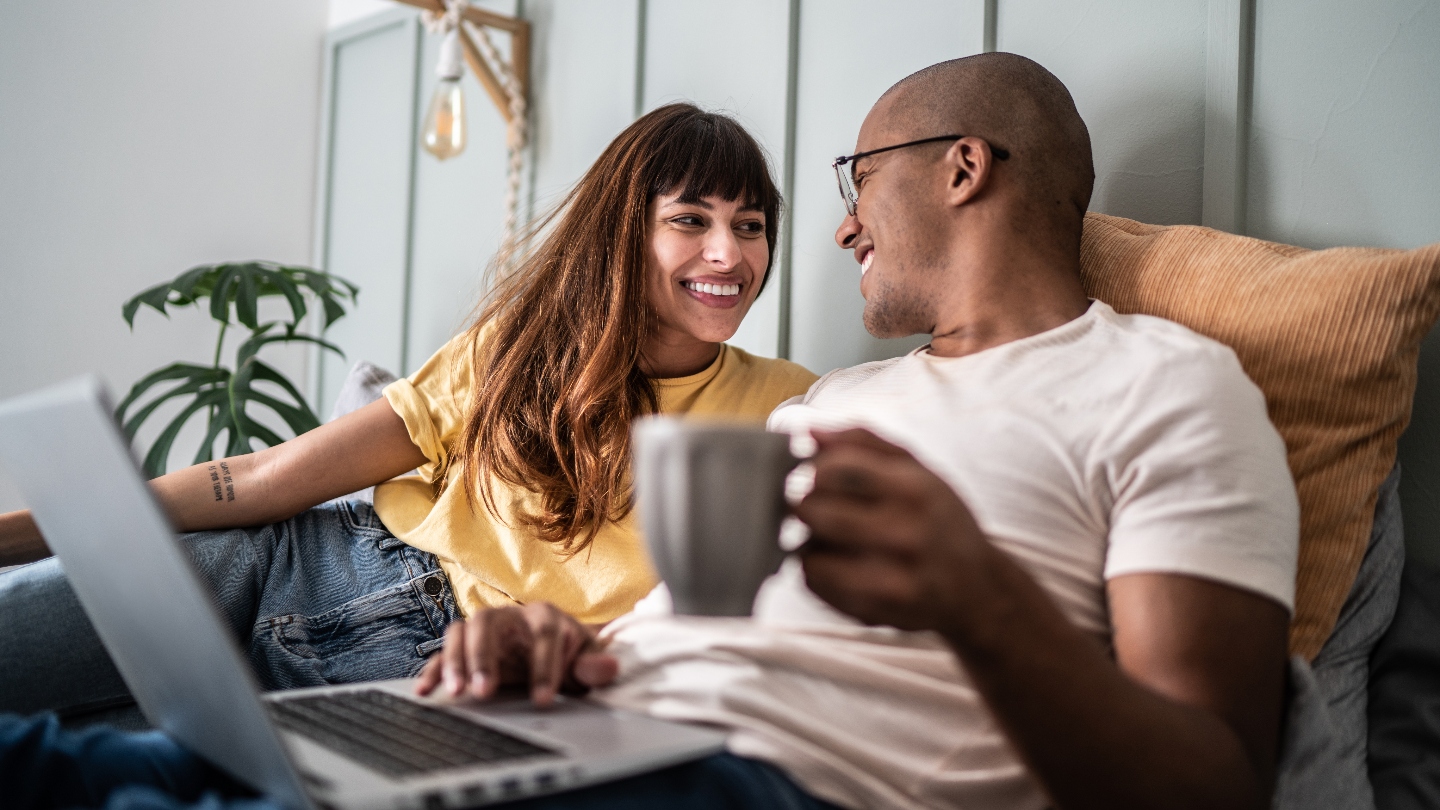 Two people sitting in bed with a computer smiling at each other