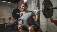 A man performing a barbell squat at the gym