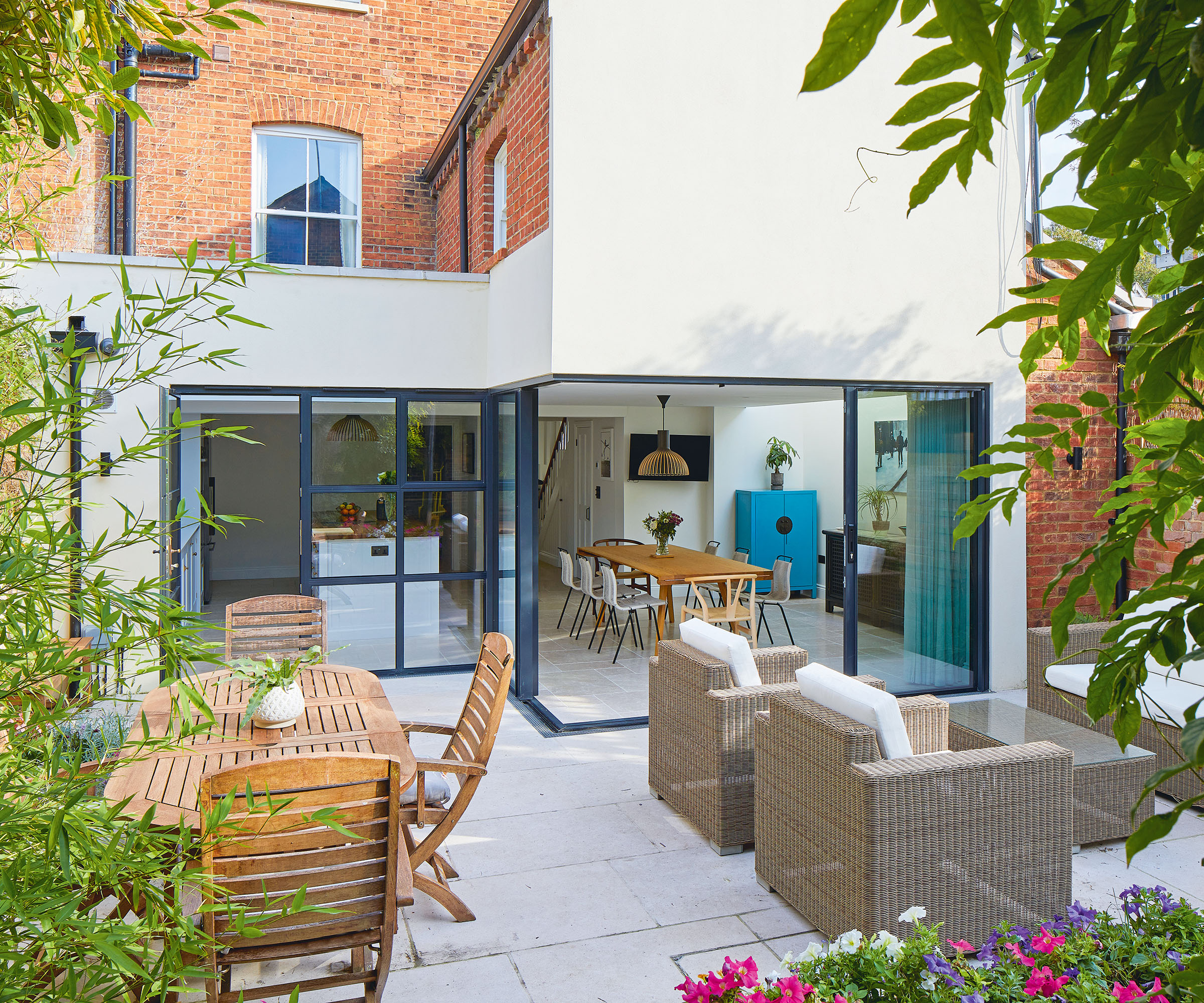 a view of a modern kitchen extension with large glass crittal doors and a patio with casual seating and a dining area