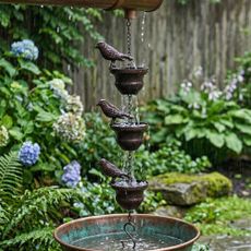 Lzvxtym Bird Rain Chain from Walmart against a backdrop of a rainy garden and water barrel