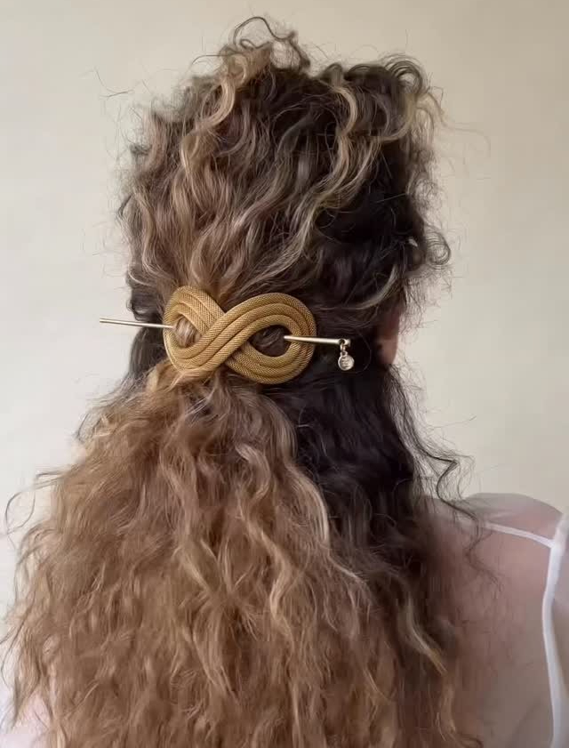 A woman with a bronde hair color, curls, and a hair pin
