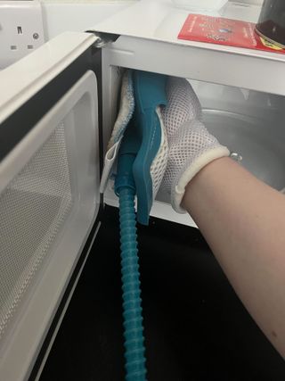 Steam cleaning the inside of a white microwave with a steam mitt