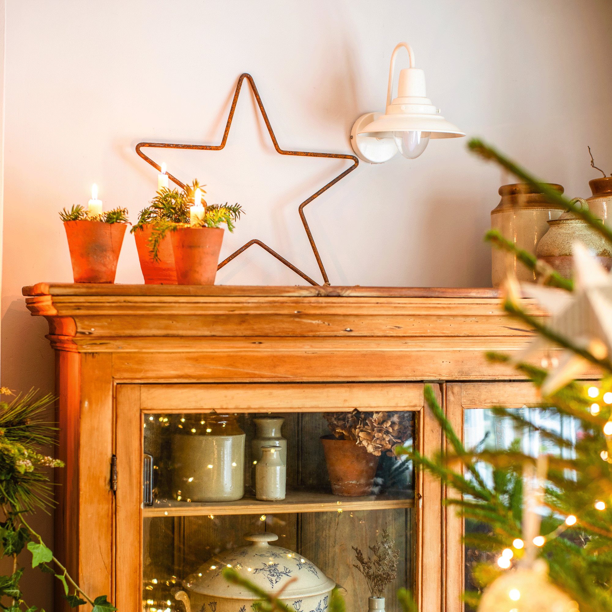a star decoration sitting on top of a glass fronted cabinet beside a Christmas tree