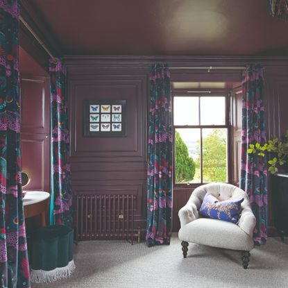 A dressing room colour drenched in an aubergine purple paint with dark floral curtains