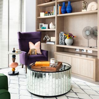 Living room with built in wooden storage and round mirrored coffee table