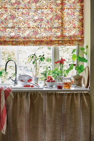 vintage kitchen sink with curtained cabinetry and floral roman blind over the window