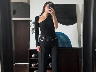 influencer alexis badiyi takes a mirror selfie wearing a longsleeve black asymmetrical top and black cargo pants.