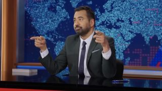 Kal Penn sitting at The Daily Show anchor desk