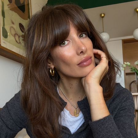 A woman with a brunette lob and fringe taking a selfie wearing a glossy lip