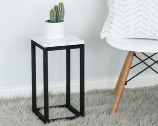 A black wooden framed DIY plant stand with marble effect top with cacti plant on top