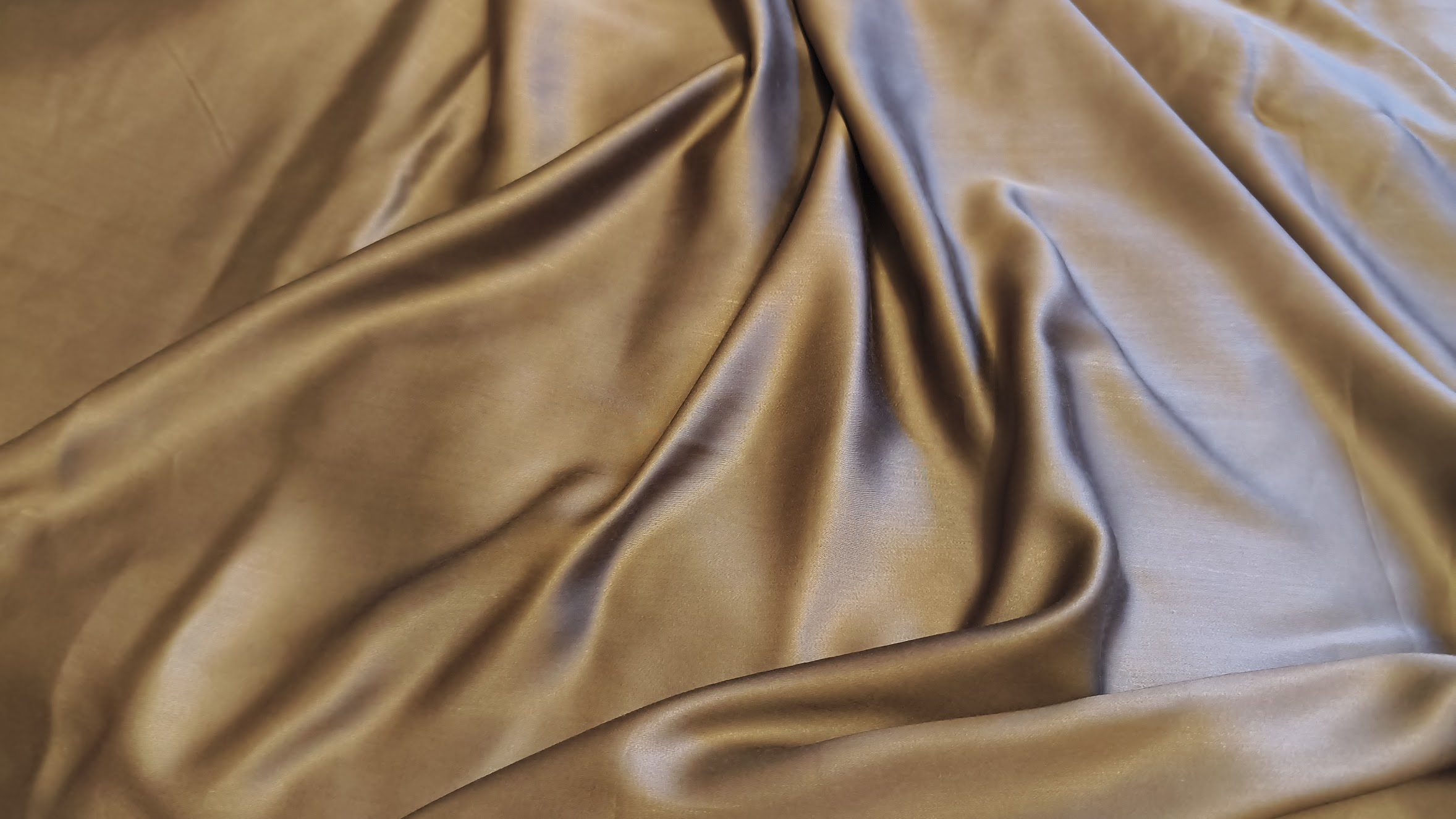 Smooth, lustrous brown fabric with a satin-like finish is draped in soft, elegant folds that capture and reflect light.