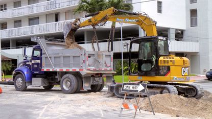 Caterpillar excavator and dump truck digging hole in street