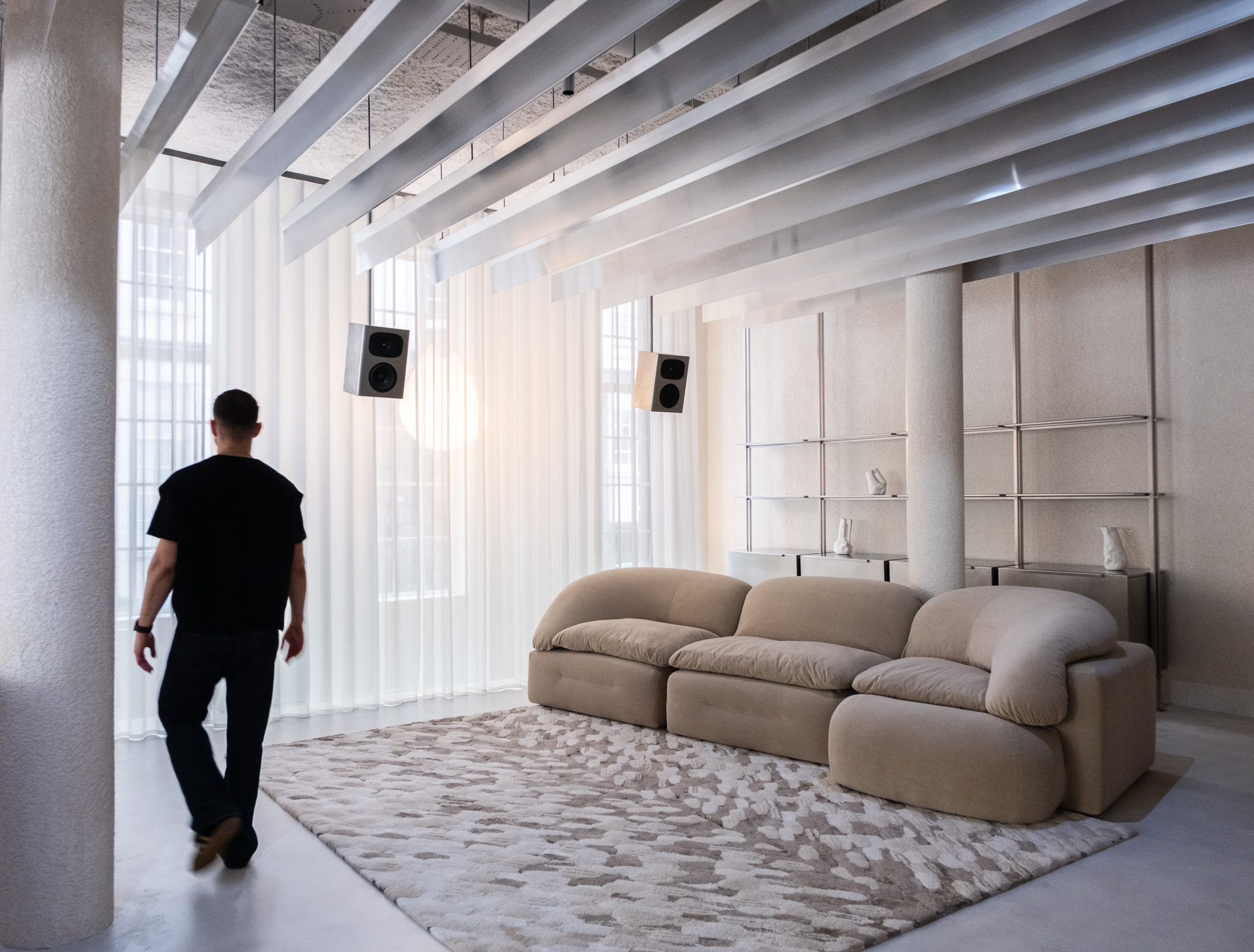 The interior of a brutalist, minial design showroom, decorated with contrasting furniture, artworks, and accessories in wood, earthy fabrics, reflective surfaces, and plants.