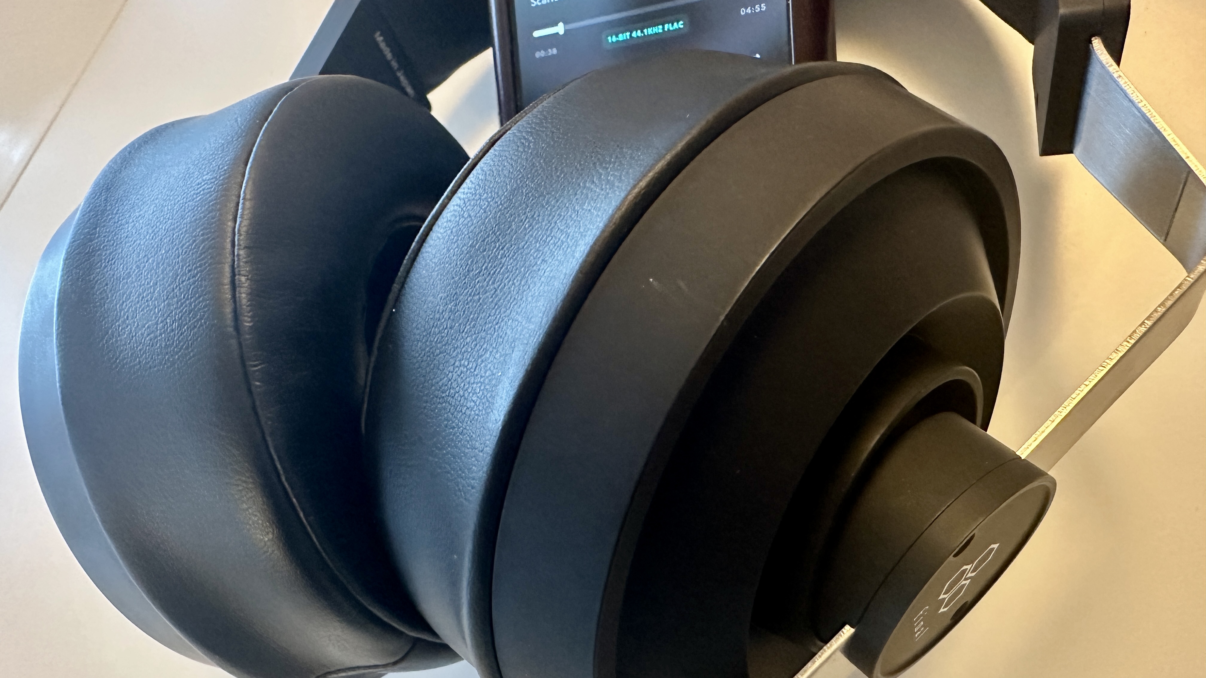 Close ups of the Final DX3000CL with a hi-res digital audio player, showing the ear cups, arm and screen on the player, all on beige background