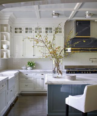 A white kitchen with a blue island and black and gold range hood