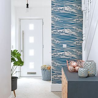 White hallway with coastal statement wallpaper on one wall and a white front door