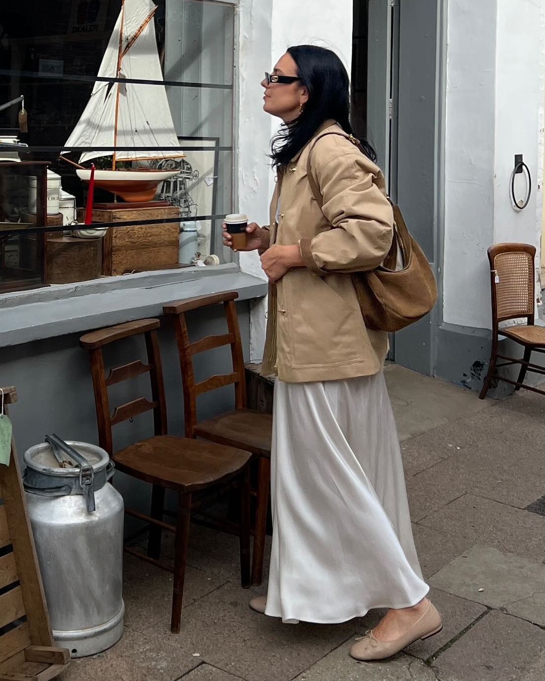 fashion influencer wearing a tan chore coat barn jacket, tan suede bag, a white slip skirt, and neutral ballet flats