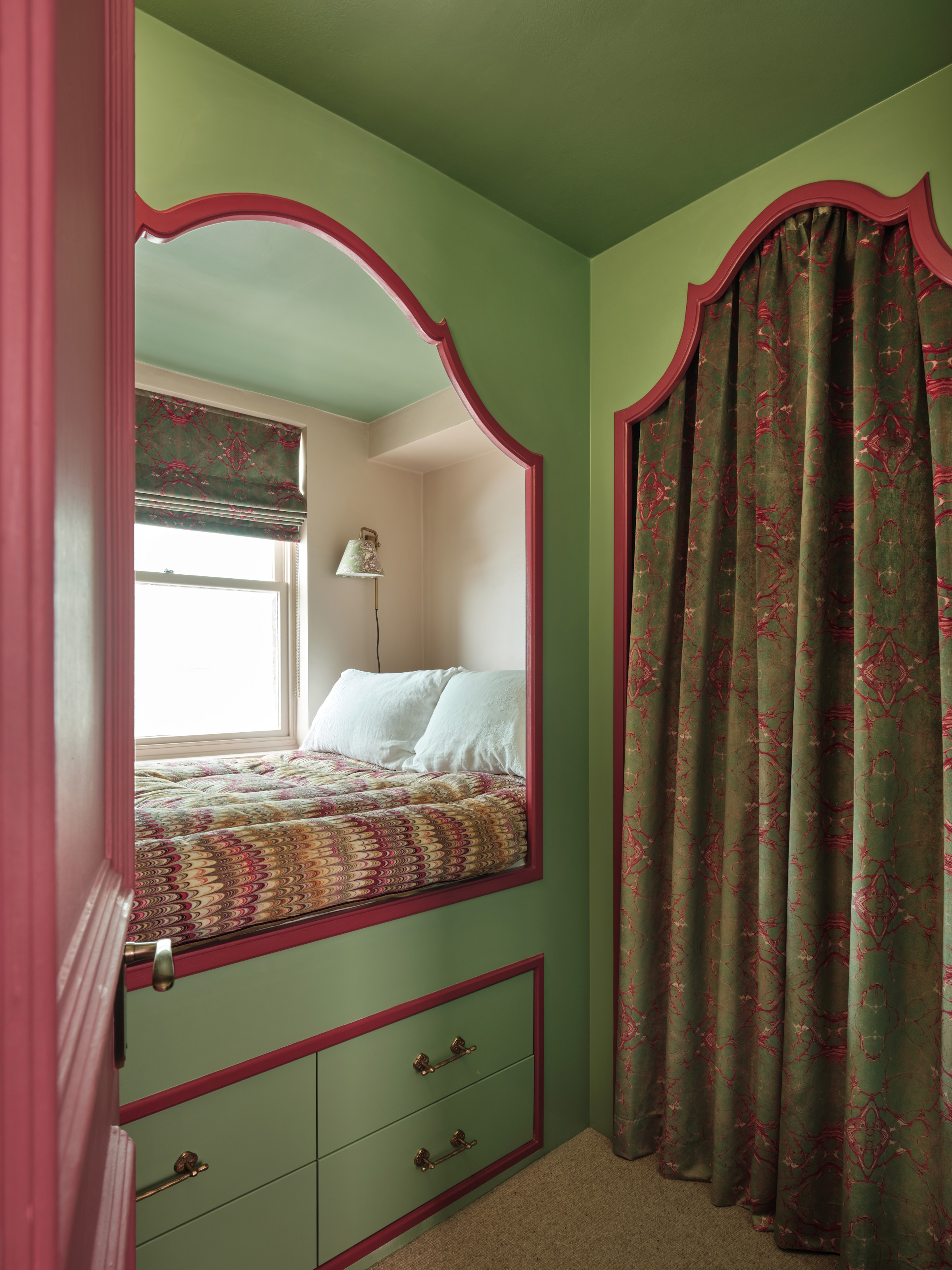 Bed built into joinery with green walls and bright pink edges