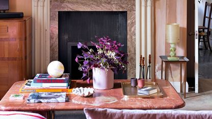 Dusty pink and purple painted wall with marble coffee table decorated with books and trays, fireplace displaying artwork