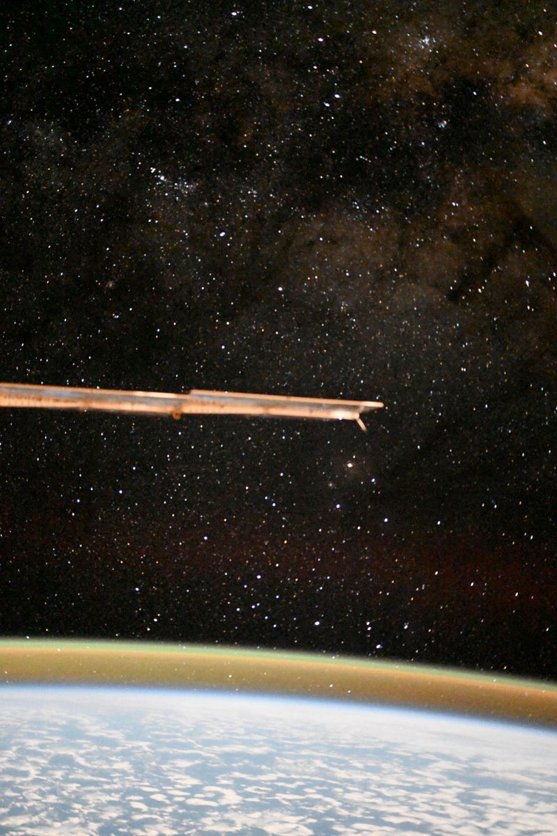 a solar array extends into the frame from the left, perforating a view of the starry sky and Earth's horizon as seen from a space station