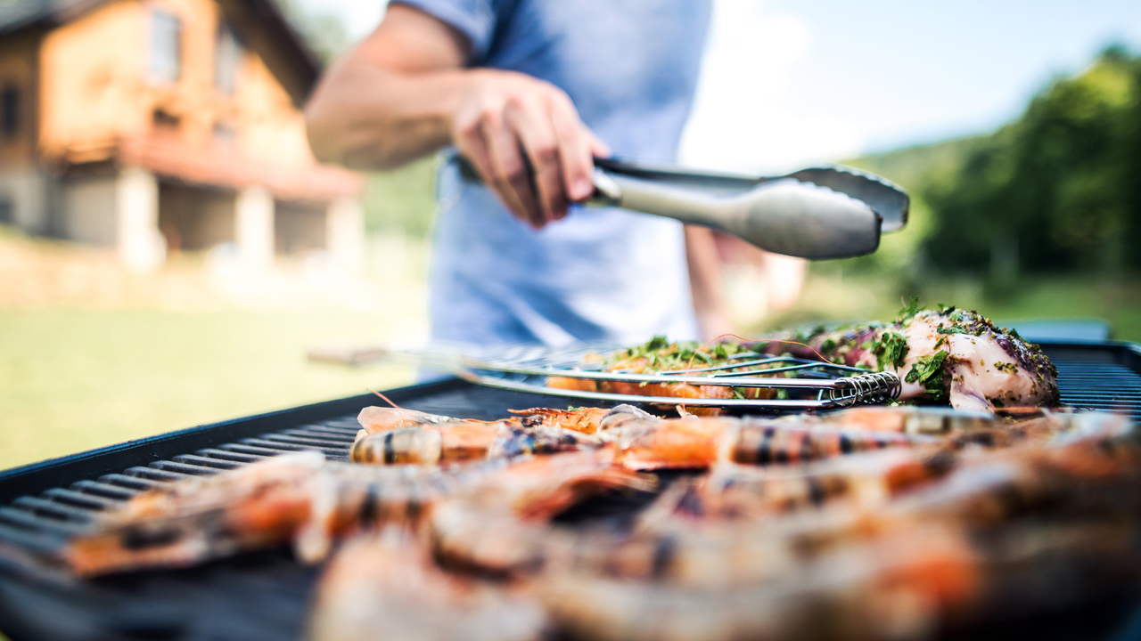 The best BBQ of 2022: Image depicts meat being cooked on BBQ and man with tongs.