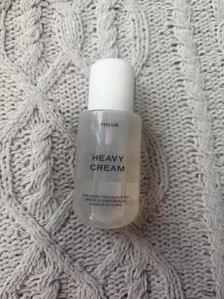 Phlur heavy cream bottle on a grey weave blanket