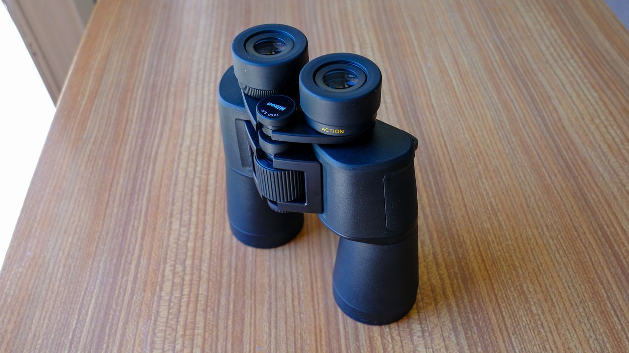 The Nikon Action 7x50 binoculars lens down stood up on a wooden table, with eyecups down.