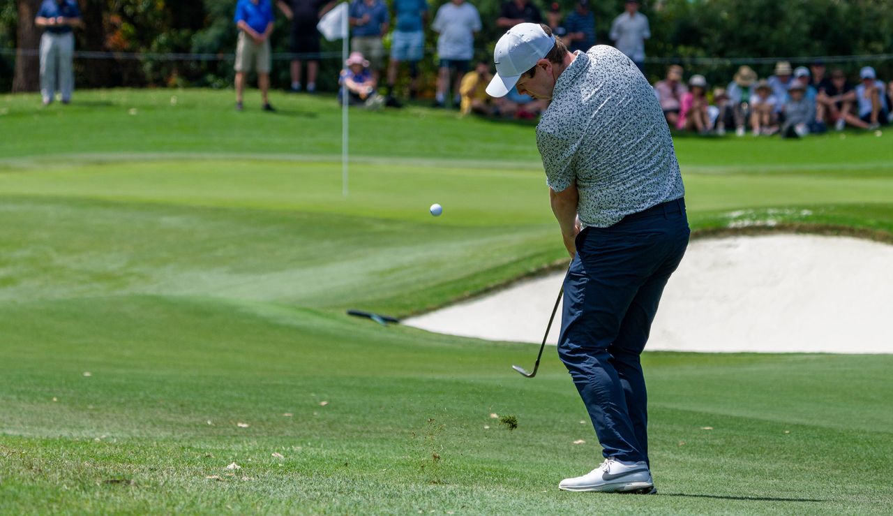 Robert MacIntyre hits a wedge shot at the flag with a bunker in front of the green