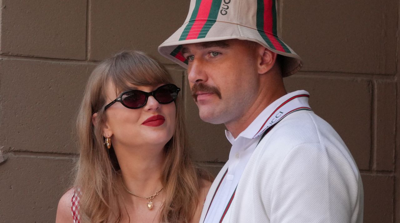 Taylor Swift, wearing sunglasses, smiles at Travis Kelce, who is wearing a Gucci bucket hat and white polo shirt