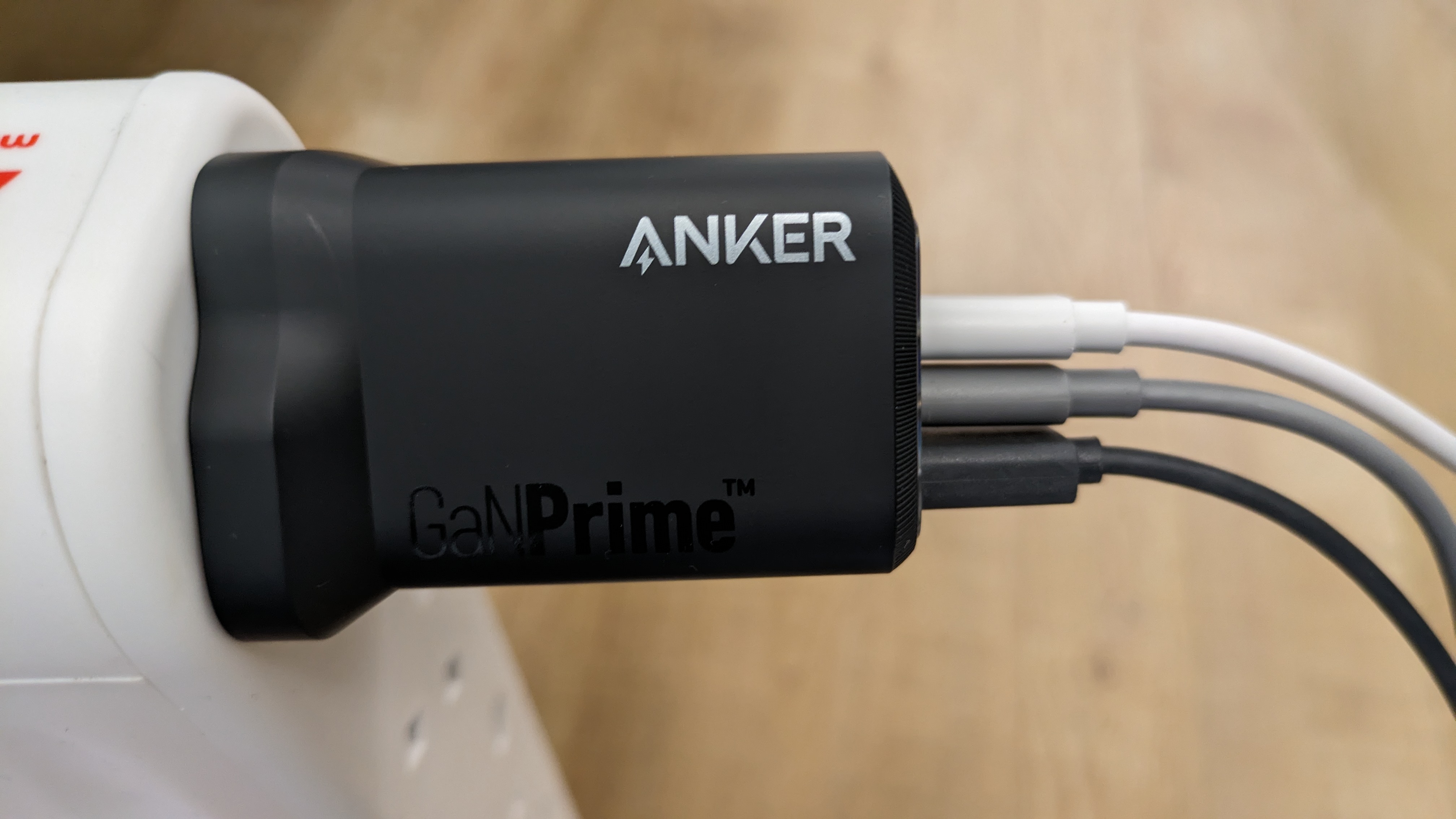 Anker Prime charger plugged into a wall socket, with three cables coming out of it